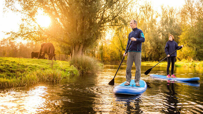 Two people paddleboarding down the River Bure