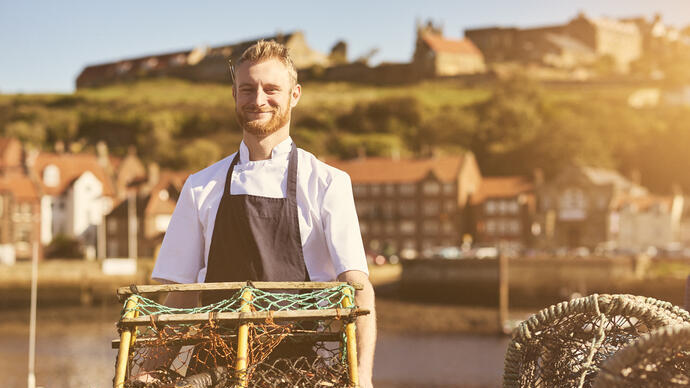 Man holding a lobster trap on a pier in the sunshine