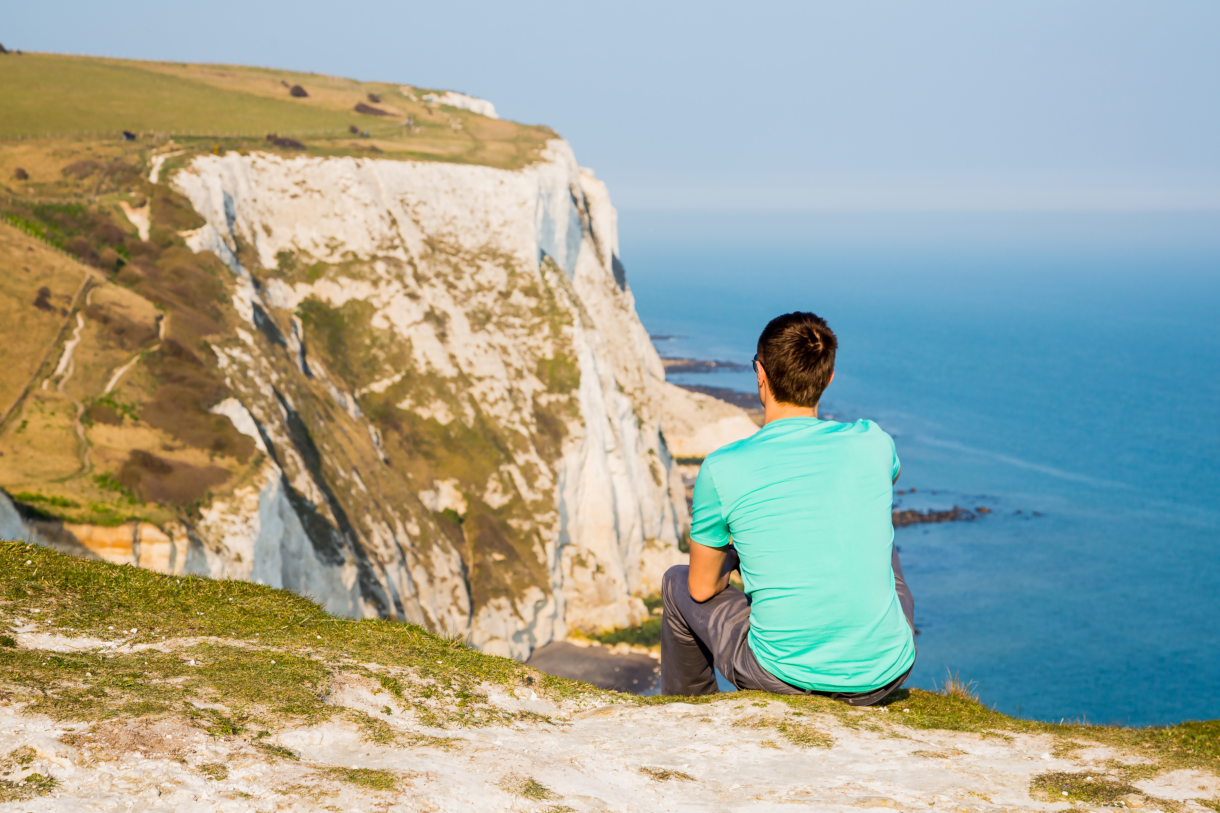 Young man sitting at the edge of the cliff near the white cliffs of Dover
