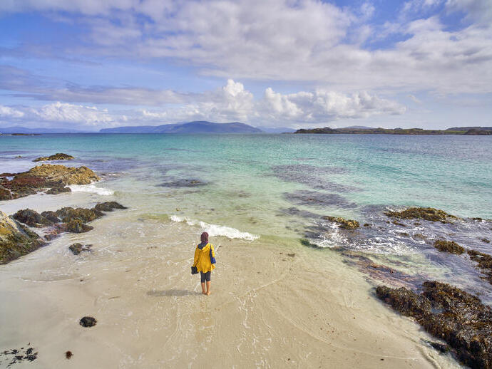 Eine junge Frau, die auf dem weißen Sandstrand mit kristallklarem, blauem Wasser spazieren geht.