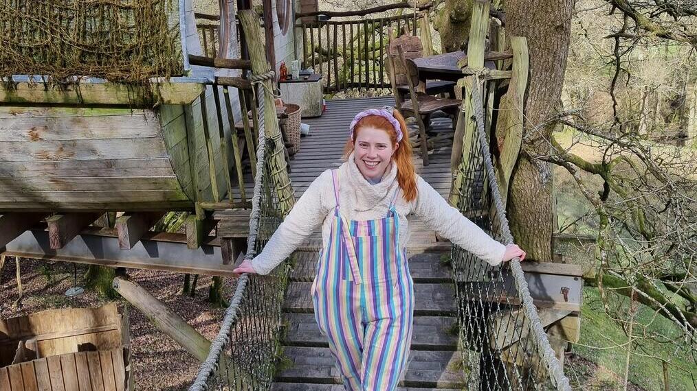 Jeune femme traversant un pont de corde depuis une cabane en bois dans un arbre