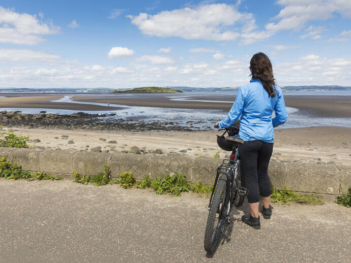 Une cycliste tenant un vélo et regardant vers une plage.