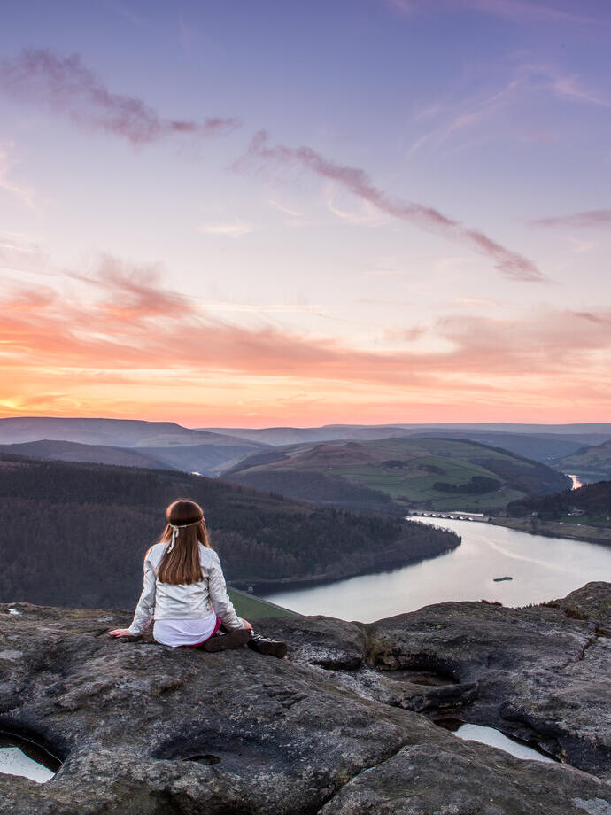 A woman sitting on rocks looking down valley to the river
