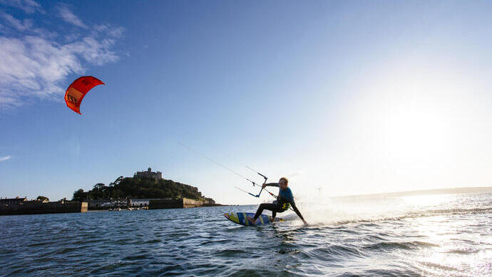 Un uomo su una tavola da surf che tiene la barra di controllo di un aquilone