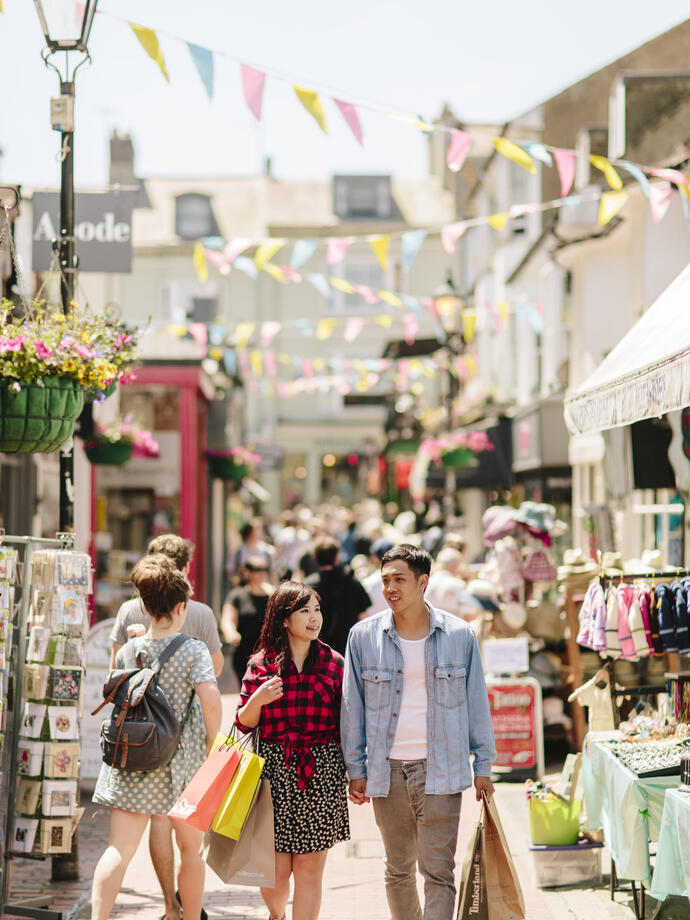 Couple holding hands, walking through a busy pedestrian street with stalls and shops either side