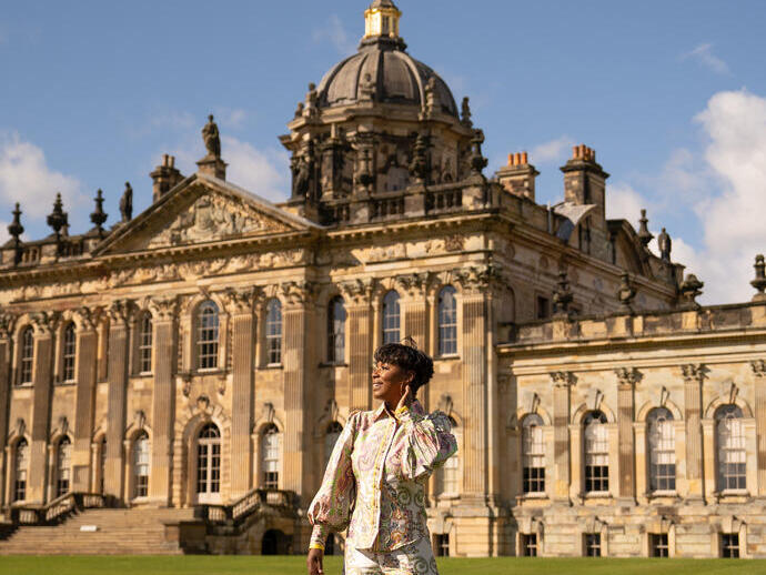 Person stands on a path in front of a grand historic building with ornate columns and a large domed roof under a blue sky.