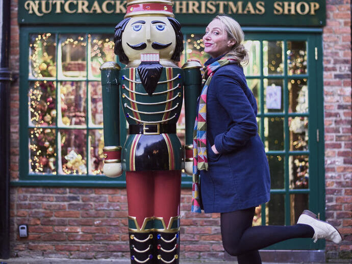 Woman posing beside a nutcracker prince statue, outside a christmas shop