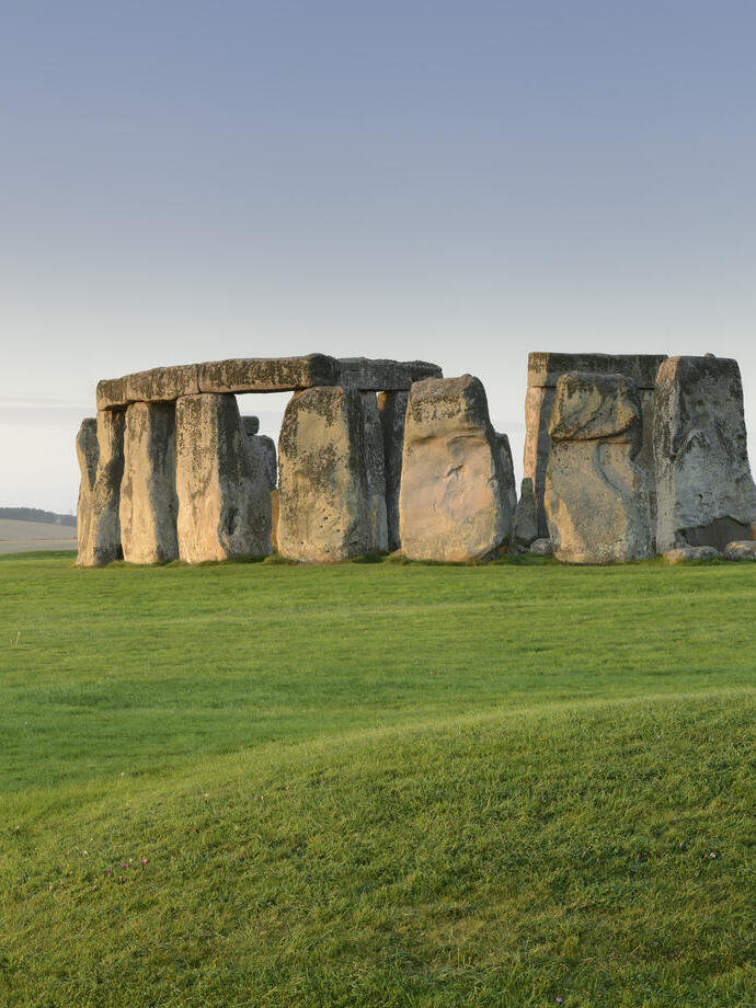 Large stone pillars arranged in circle on grass at sunset