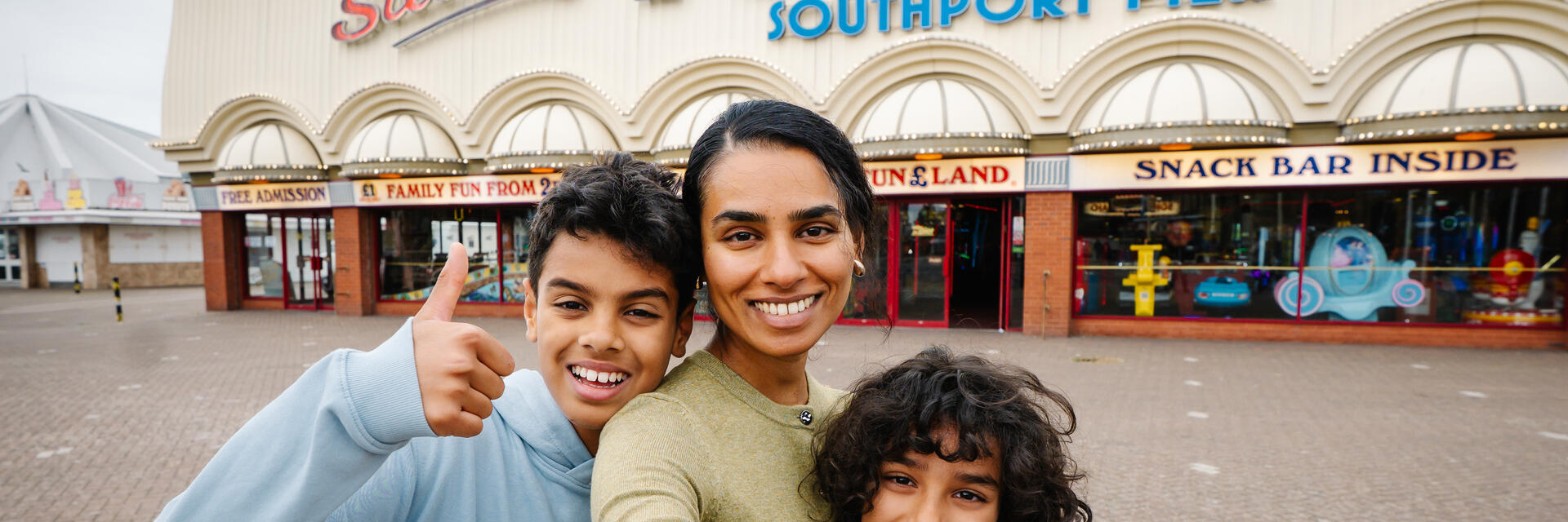 A mother and two sons stand outside an amusement park