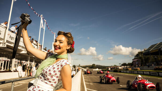 Woman taking a selfie in vintage dress standing by a car racing track