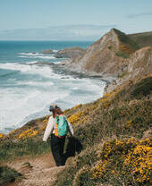 A woman walks along a coastal path with sea and headland in the distance