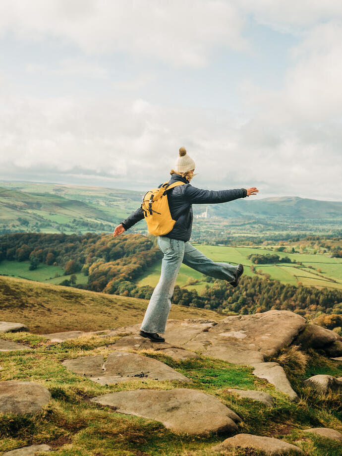 Woman skipping on rocks at edge of hill. Landscape view