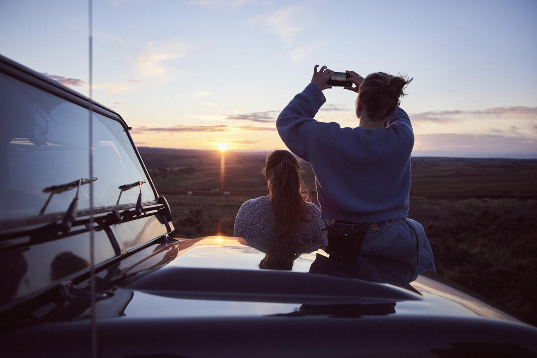 Deux femmes près d'une jeep garée regardant le coucher de soleil à l'horizon