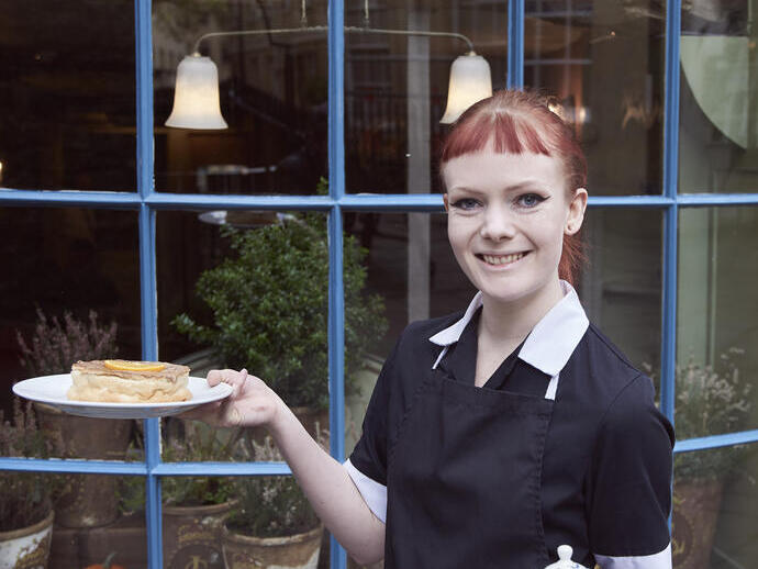Empleado de restaurante sosteniendo una bandeja con té y un pastel en un plato