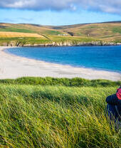A woman sitting in grass overlooking a spit and fields