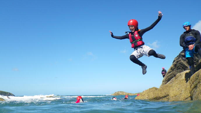 Eine Person, die bei einem Coasteering-Abenteuer bei Celtic Quest in Pembrokeshire, Wales, ins Meer springt