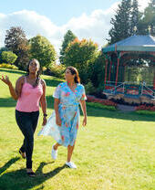 Two women walking on grass past a pergola
