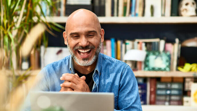 Cheerful handsome mature man at home speaking on video call using laptop