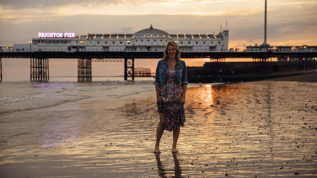 Mujer de pie en la playa cerca del muelle al atardecer