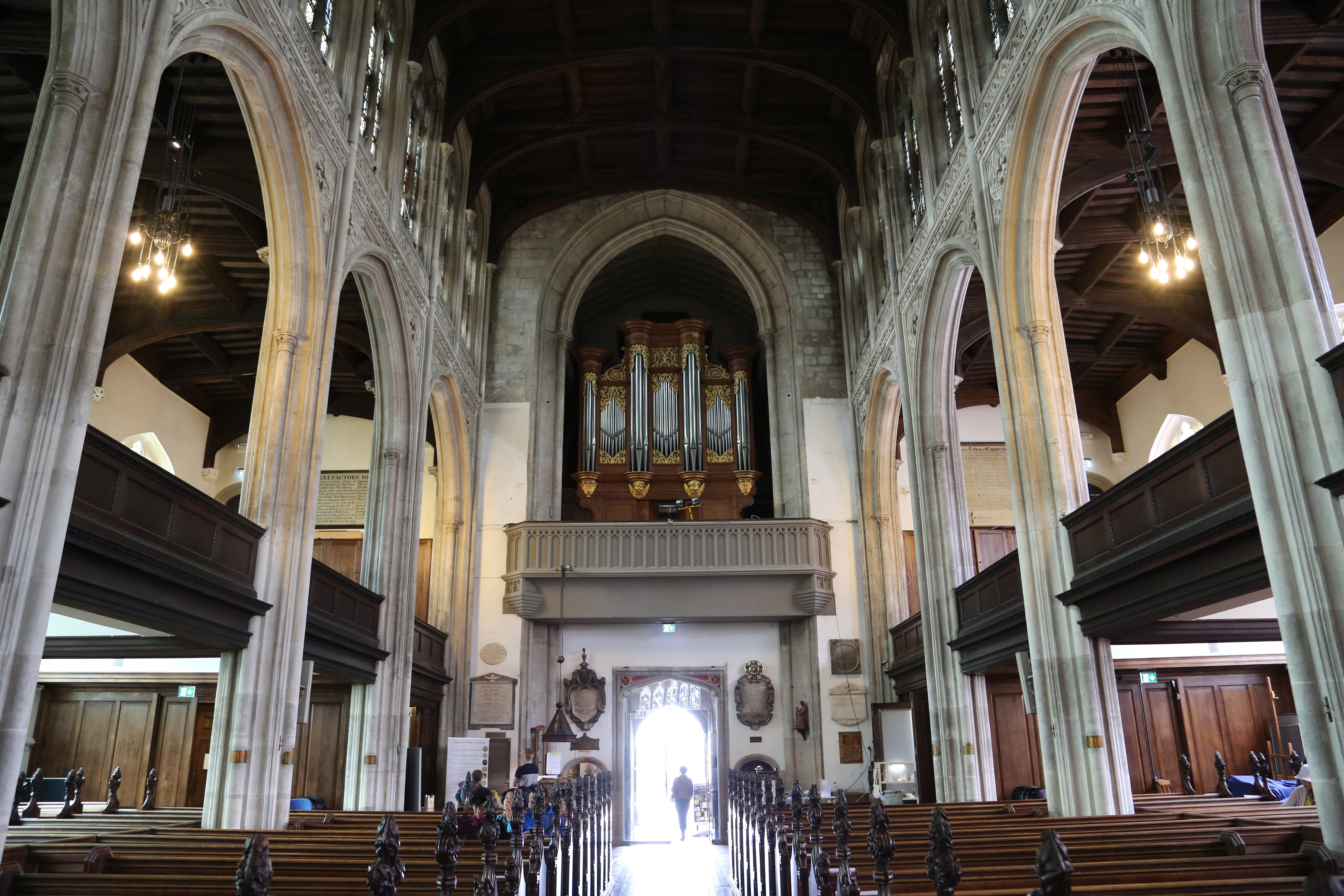 Interior of a historic church with stone arches, wooden pews, a pipe organ above the entrance, and vaulted wooden ceiling.