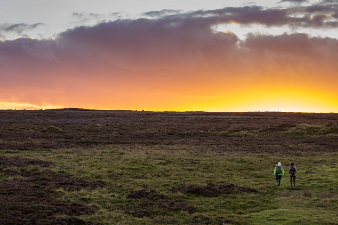 Dos amigos caminando hacia la puesta de sol sobre la colina