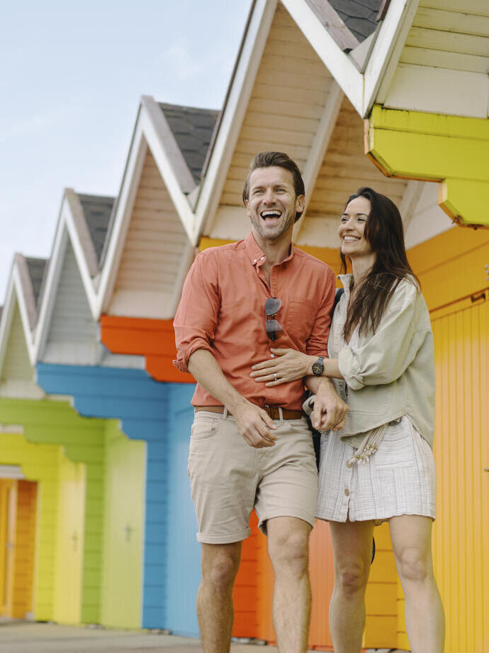 A man and woman laughing outside colourful beach huts