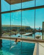 Une personne nageant dans une piscine thermale, entourée de baies vitrées