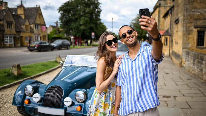A man and a woman take a selfie in front of a classic car