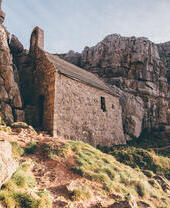 An old brick building on a hill, surrounded by cliffs.