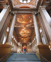 Man walking up a grand staircase towards a large hall with a painted ceiling