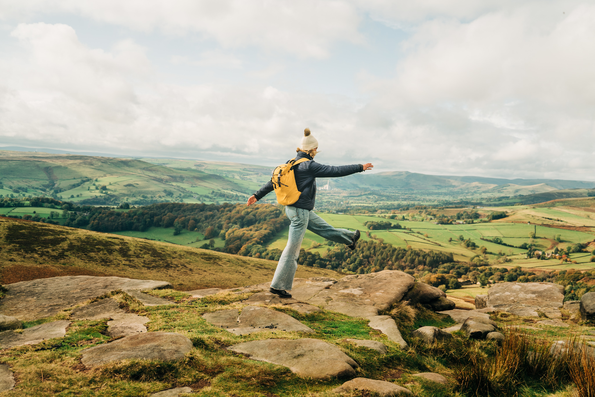 Woman skipping on rocks at edge of hill. Landscape view