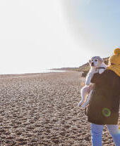 A woman carrying a dog along a beach in Dunwich