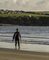 Une personne marchant sur une plage avec une planche de surf sous le bras