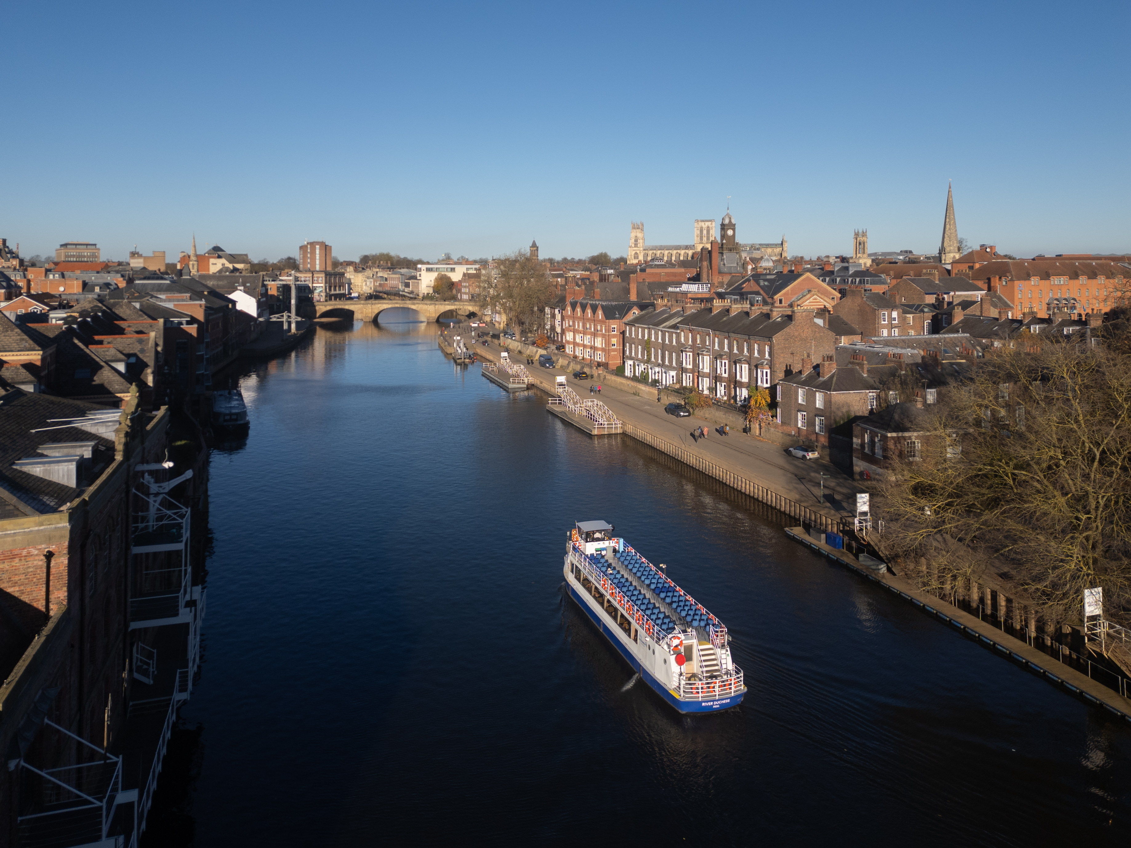 A boat travels down a river towards a bridge with the City beyond
