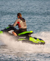 Middle aged man wearing a life vest rides a personal water craft Jet Ski along a calm sea.
