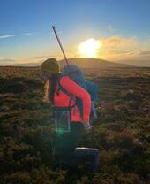 Female hiker with a backpack and walking poles, hiking through the countryside of Kilder in Northumberland at sunrise