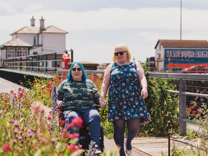 A woman walks with another women who sits in a wheelchair at an old railway station