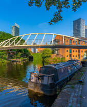 Bateau amarré sur un canal avec un pont piétonnier et des immeubles en arrière-plan