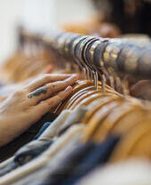 A close up shot of hands sifting through clothing hanging on a clothes rack in a clothes shop.
