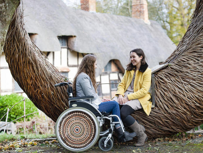 Wheelchair user and friend sat beside a wooden sculpture