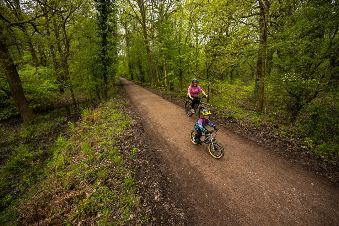 Mutter und Sohn fahren auf einem Waldweg durch Bäume.