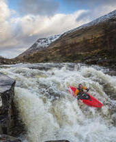 Kayaker, in a red kayak, going over raging rapids