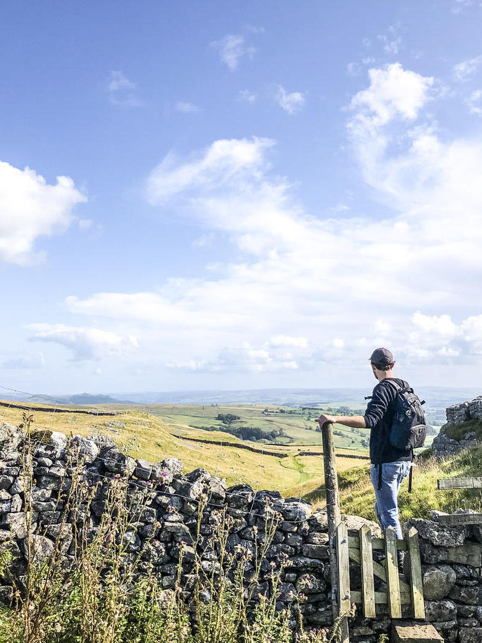 Man standing on stile over stone wall looking at landscape