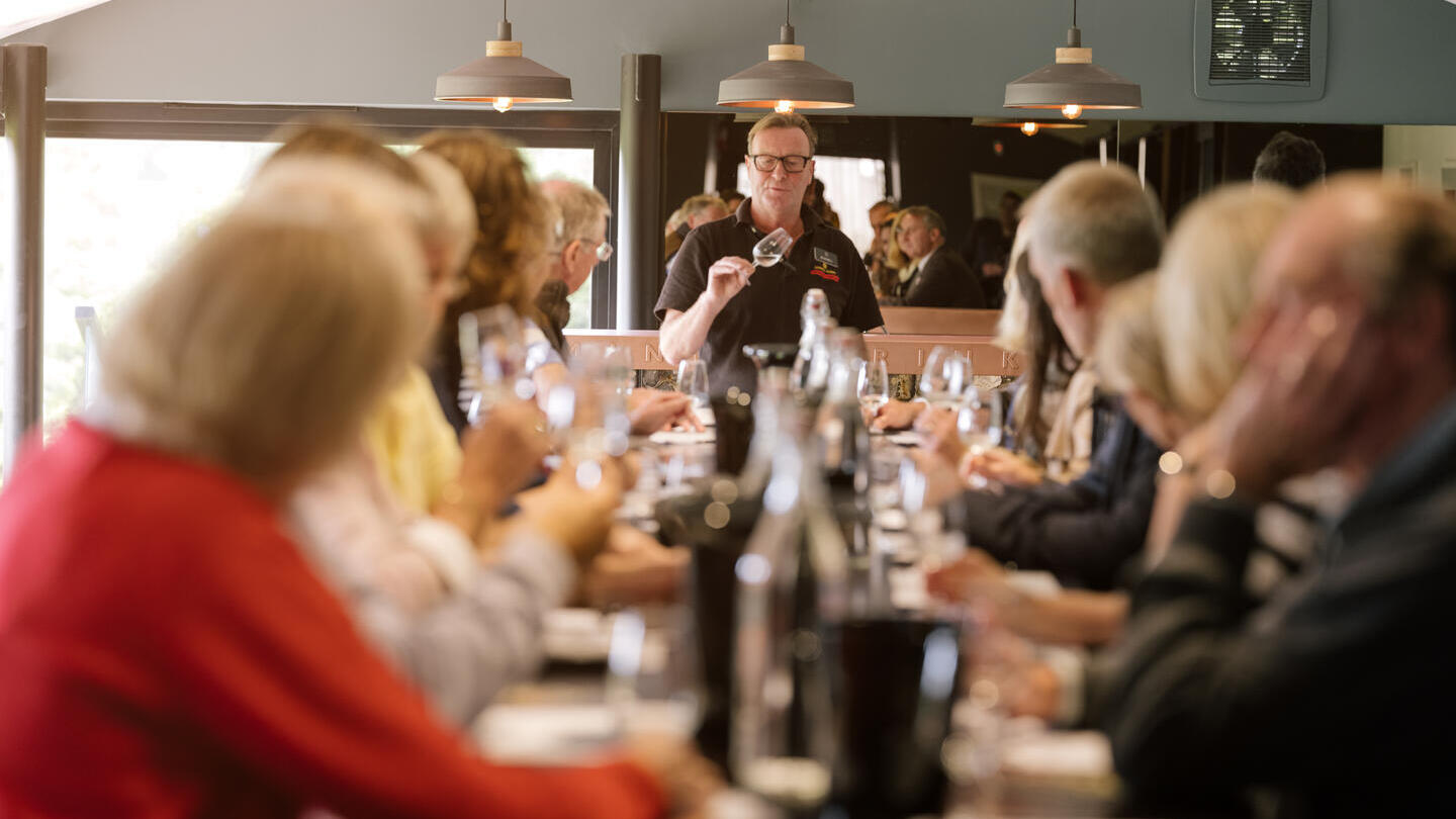 Grand groupe de personnes assises à une longue table lors d'une dégustation de vins.