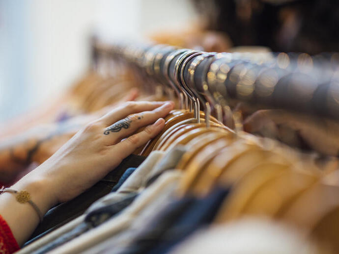 A close up shot of hands sifting through clothing hanging on a clothes rack in a clothes shop.