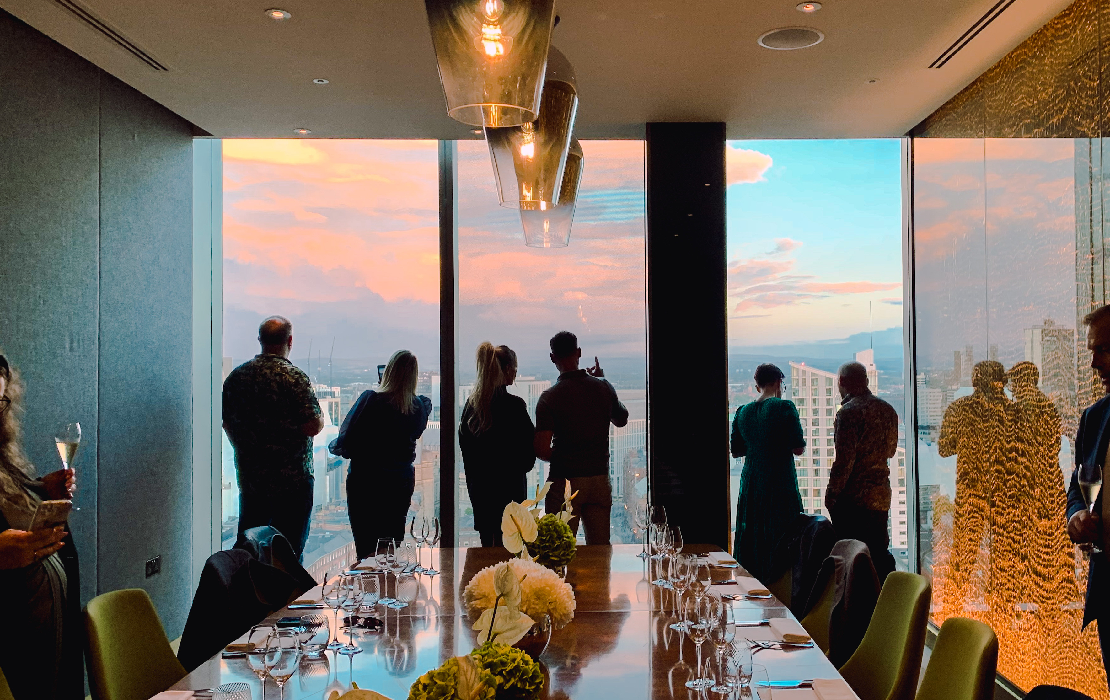 A group of people drinking while looking out over Manchester's skyline in a private room at 20 Stories Restaurant
