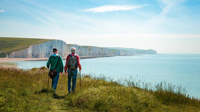 Two men hiking together with the stunning backdrop of white cliffs overlooking the ocean.