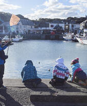 Children sat on a harbour wall fishing for crabs