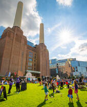 Una foto exterior de la central eléctrica de Battersea bajo el sol, rodeada de familias y grupos de personas