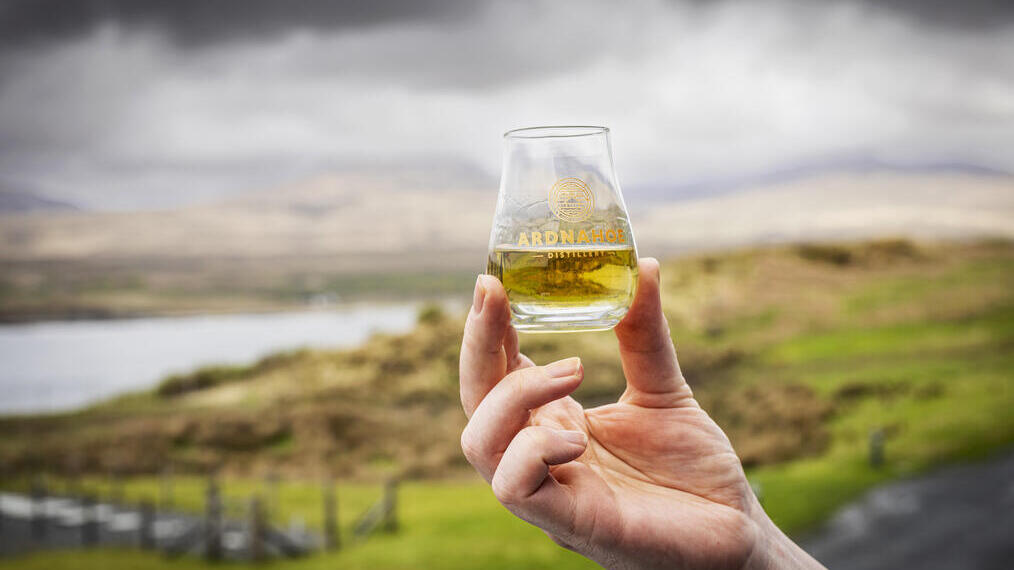 Man holding glass of whiskey with loch in the backround